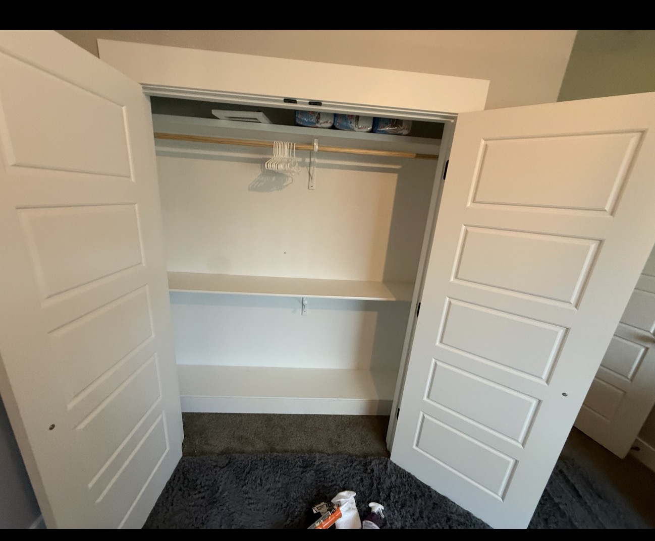 Installed white paneled closet doors with shelves and hanging rail
